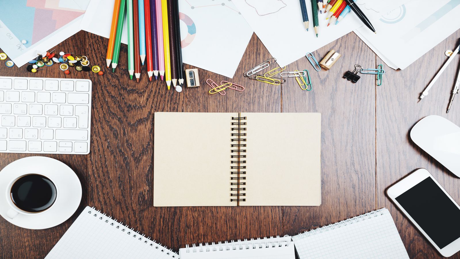 A desk with multiple open notebooks, each showing a different project plan, connected by hand-drawn lines